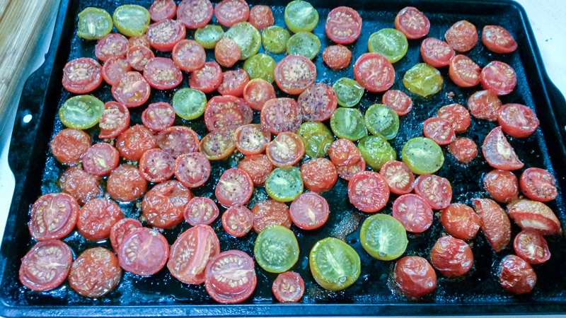 Roasted cherry tomatoes sliced in half, on roasting pan