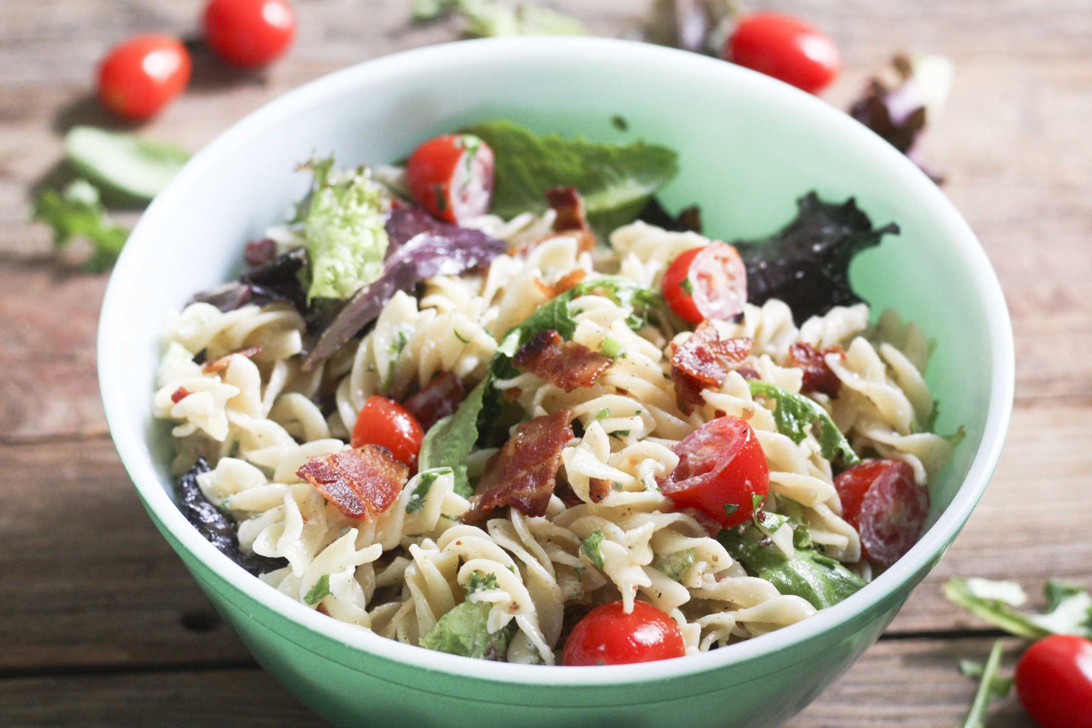 BLT Pasta Salad in green bowl with chunks of bacon on top 
