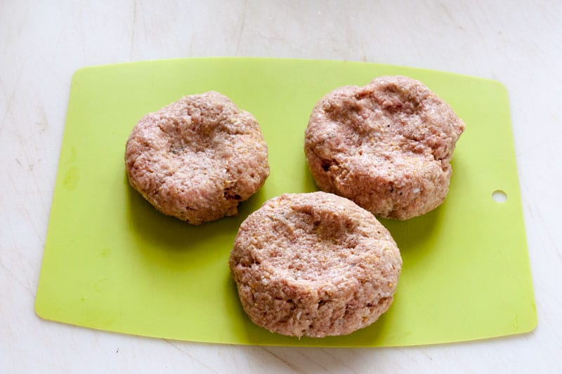 shaped raw turkey burgers on green plastic cutting board