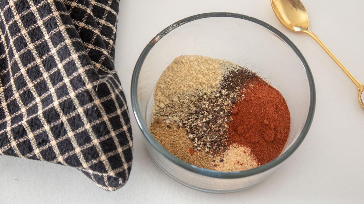 All spices in glass bowl. Adobo seasoning in glass bowl with gold spoon.