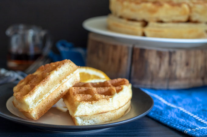 Individual waffles on plate with whole waffles in bacground on wood round