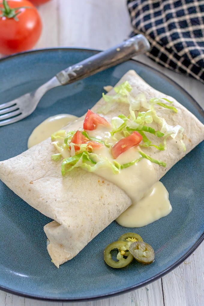 Burrito with cheese sauce garnished with tomatoes and lettuce