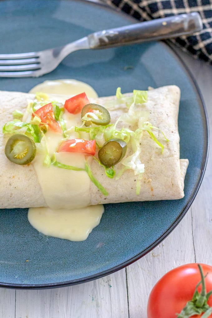 cheese sauce on burrito garnished with jalapeno pepper slices 