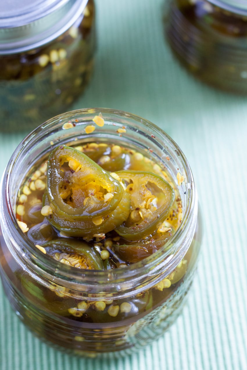 candied jalapenos in an opened jar with jars in background