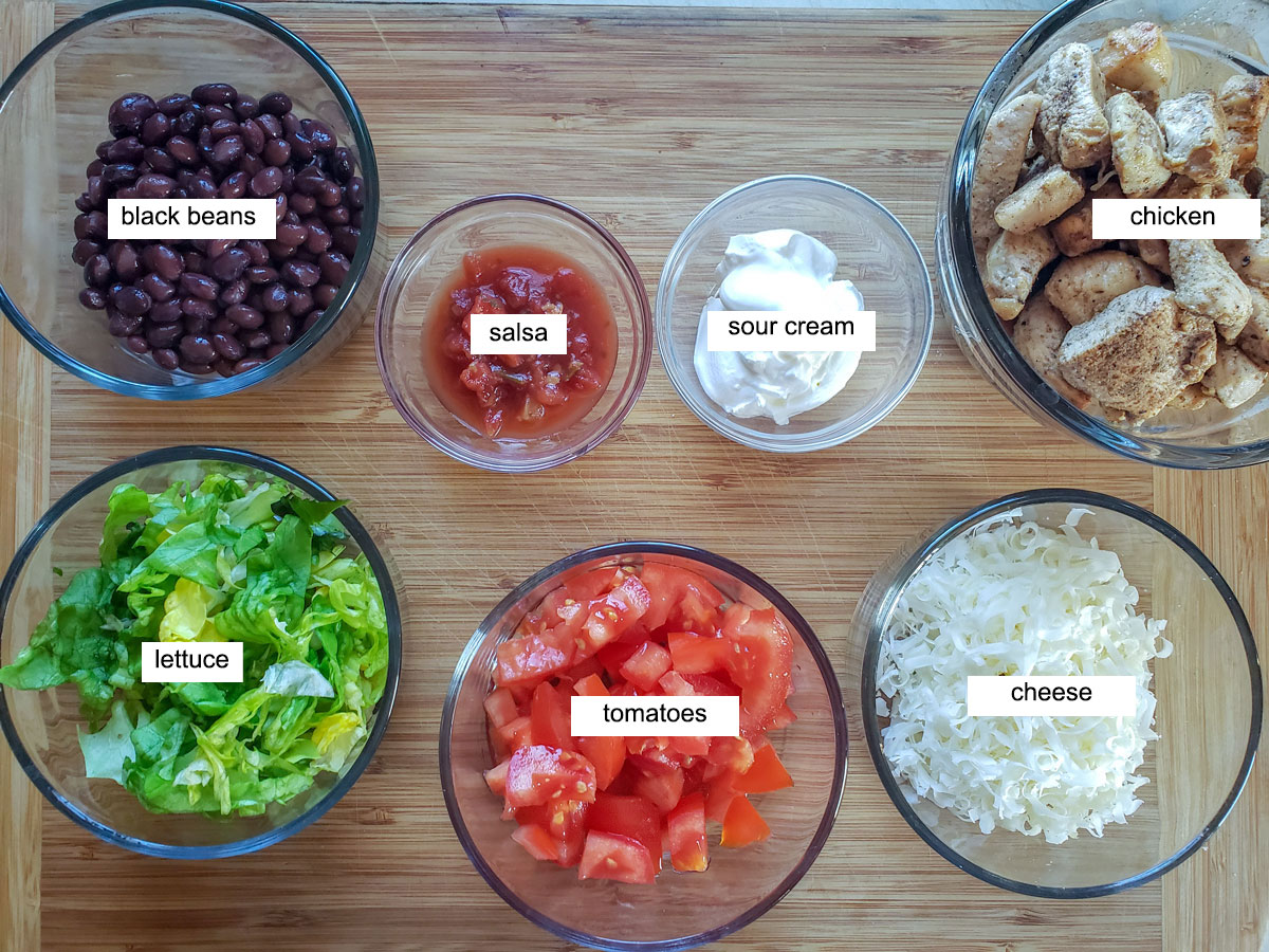 Ingredients for chicken nachos, Chicken, beans, lettuce, tomato, cheese on bamboo board.