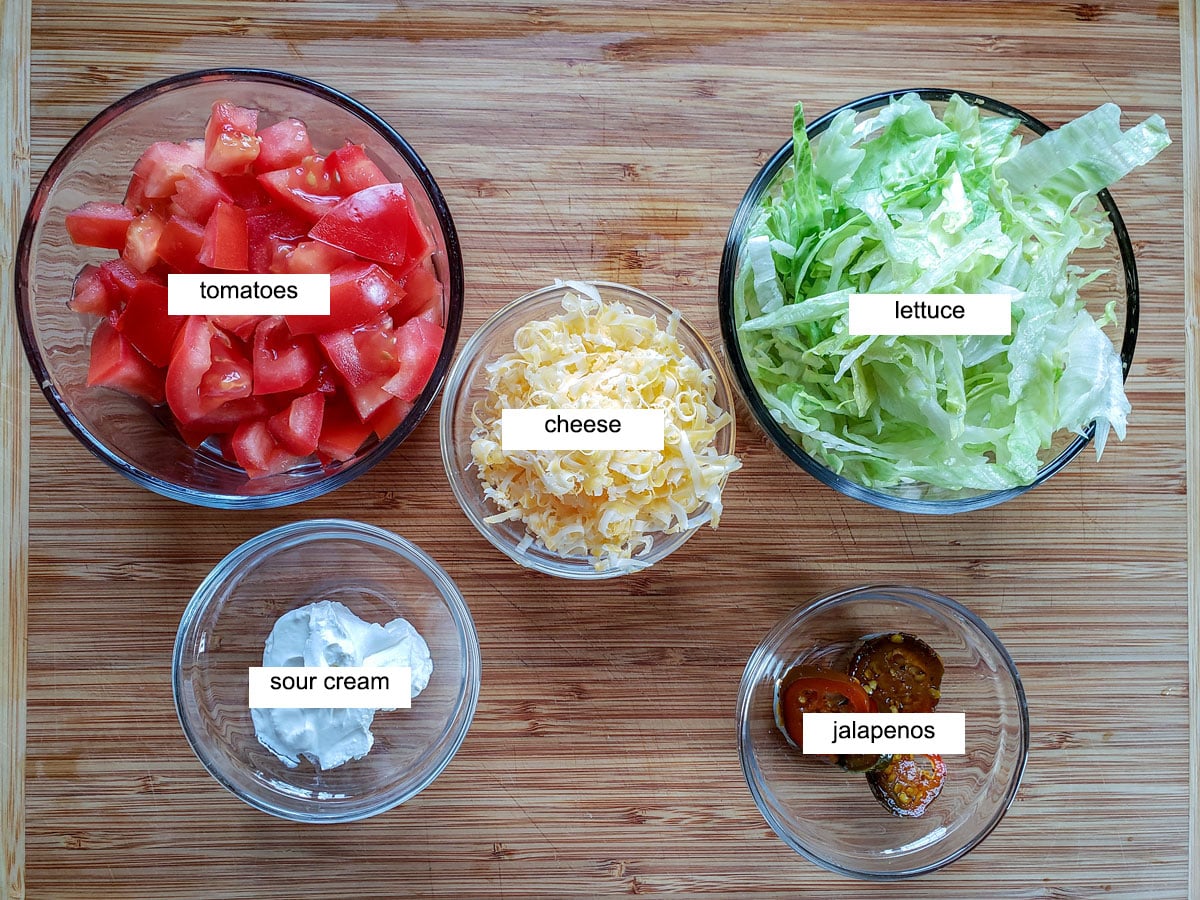 chopped tomatoes, sour cream, jalapenos, lettuce and cheese on board.