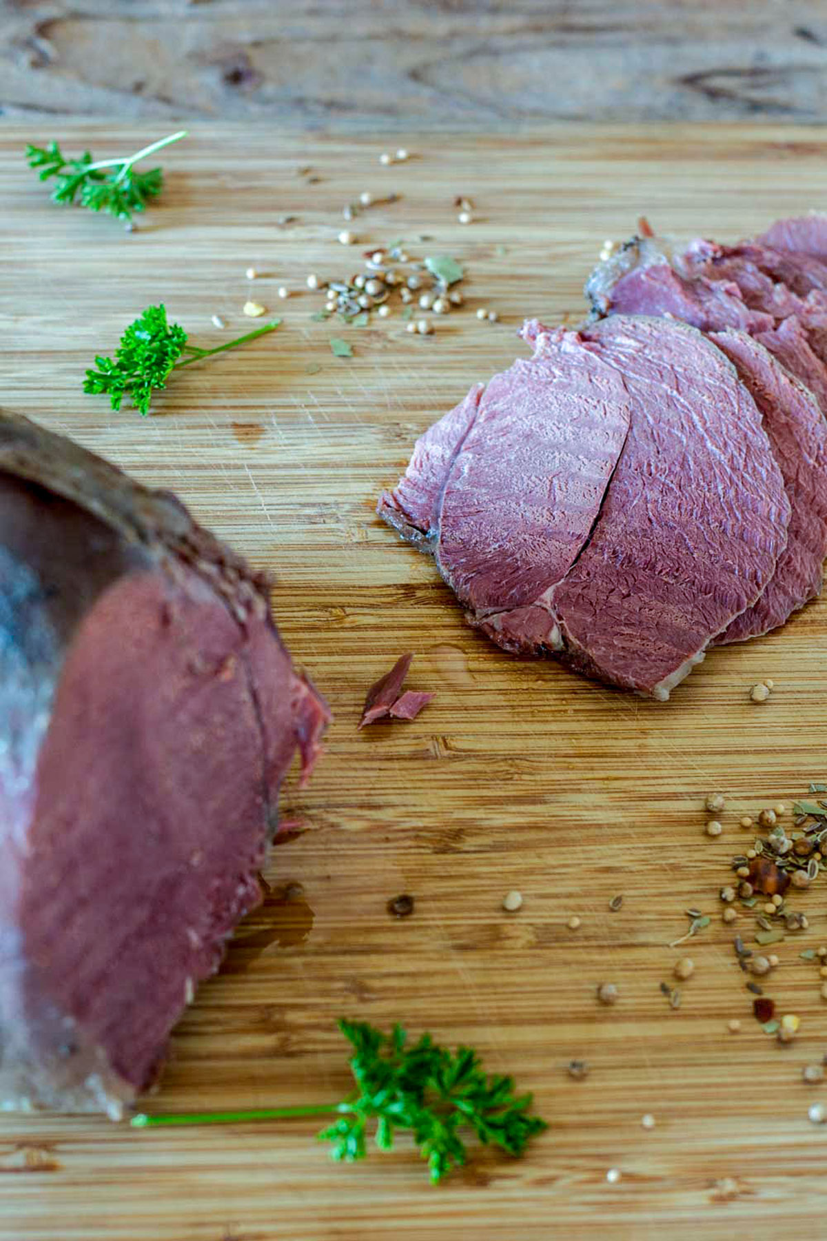 slices of corned venison on wooden board with pickling spices