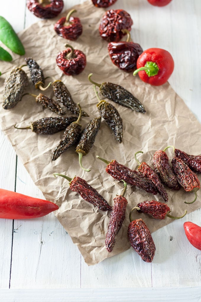 dried peppers next to fresh peppers on paper.