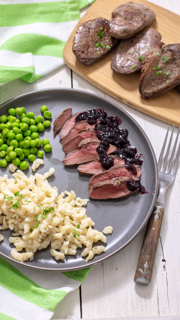Sliced duck breasts with blueberry sauce on grey plate.