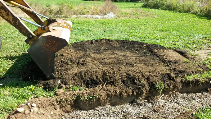 Backhoe bucket digging soil to plant garlic