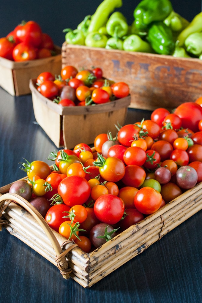 basket full of red tomatoes next to basket full of green peppers
