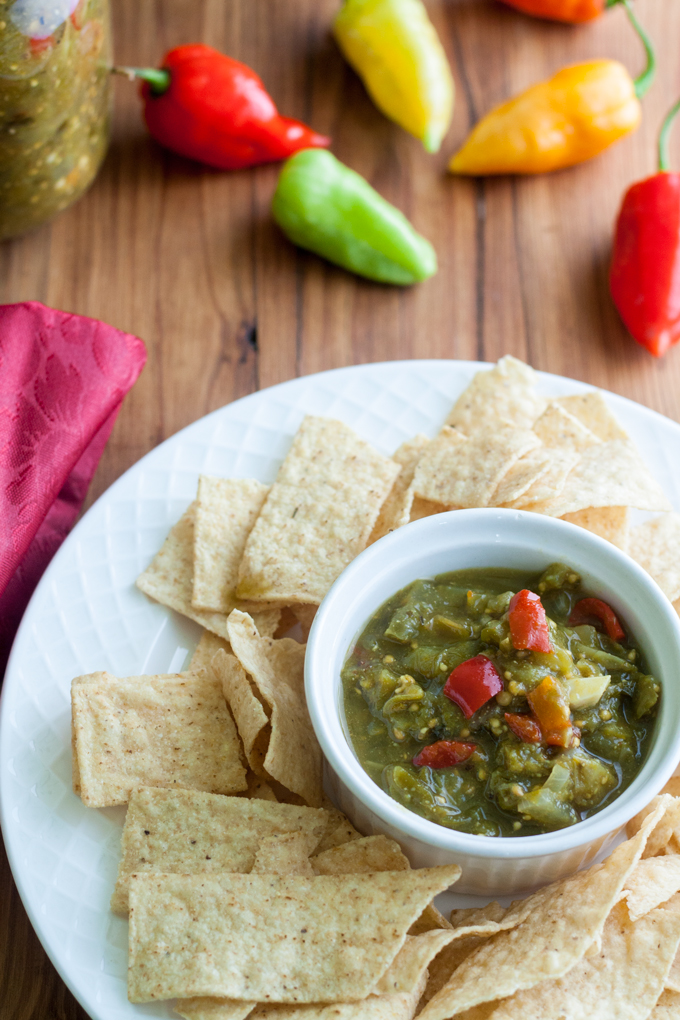 white ramekin filled with green tomato salsa on white plate surrounded by tortilla chips