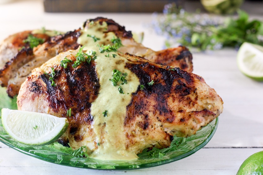 Whole grilled chicken breast on green platter with curry sauce on top