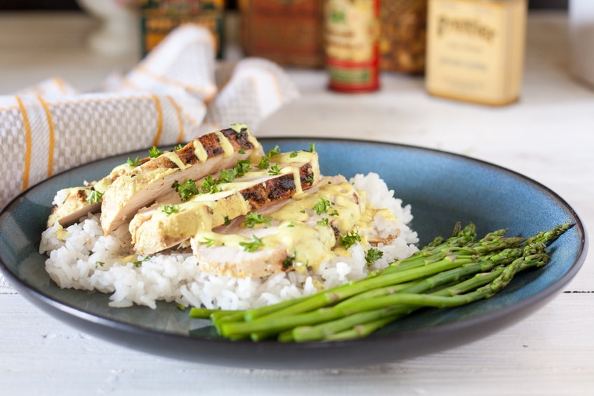 sliced chicken breast pieces on bed of rice with curry sauce on top and asparagus on the side