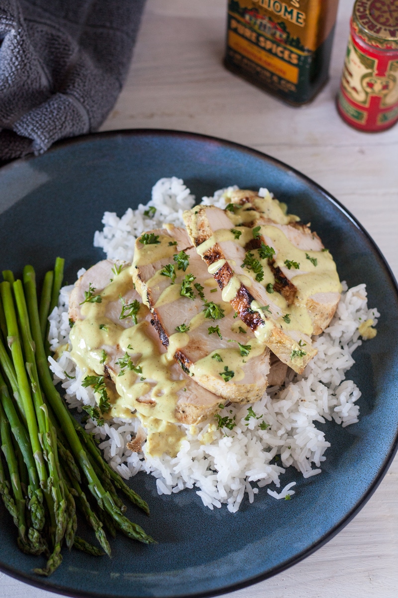 sliced grilled chicken on bed of rice topped with lime coconut curry sauce on white plate