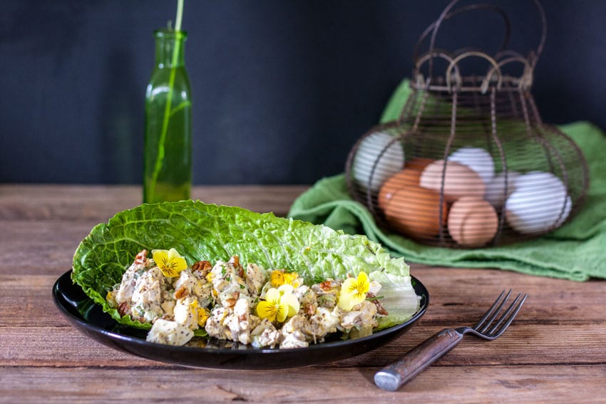 grilled chicken salad with large chunks of pecans and eggs, served on large lettuce leaf garnished with edible yellow pansies
