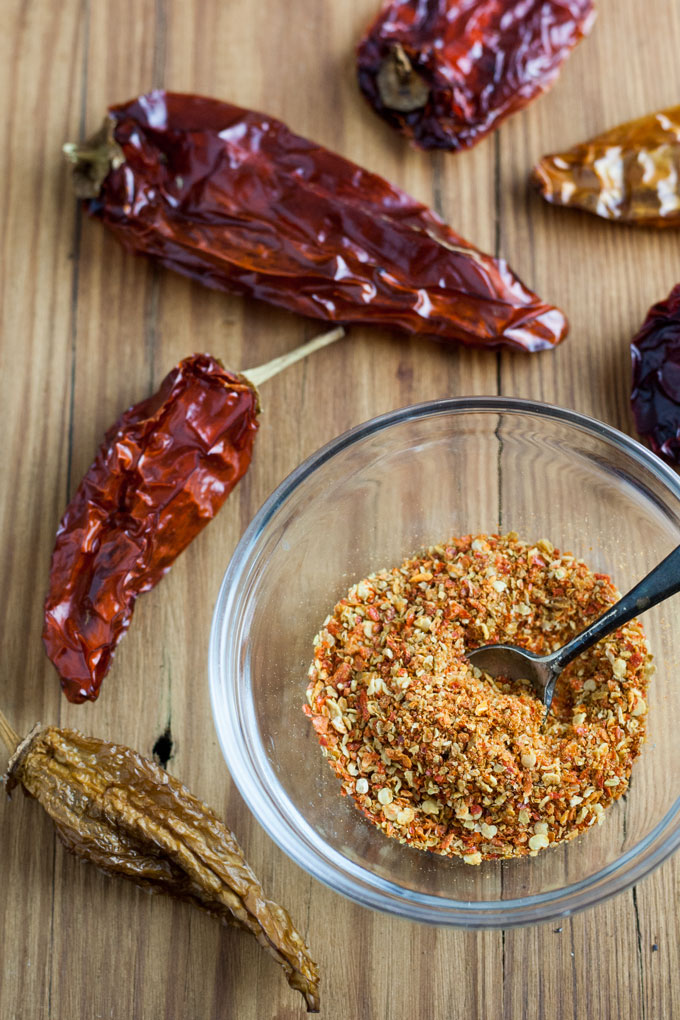 glass bowl with crushed peppers and small spoon next to dried peppers