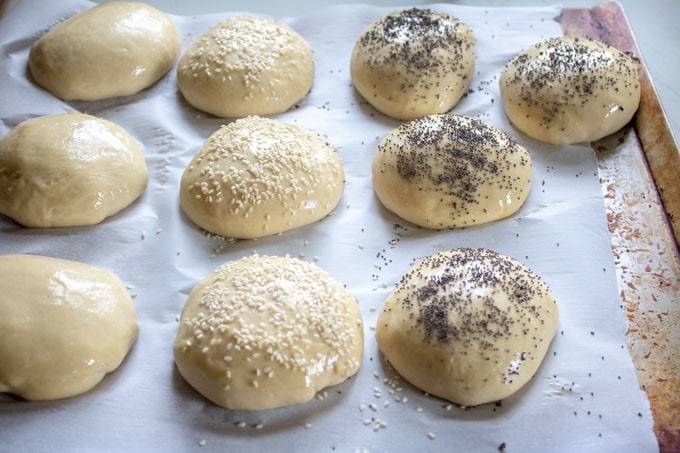 unbaked hamburger buns on parchment, sprinkled with seeds.