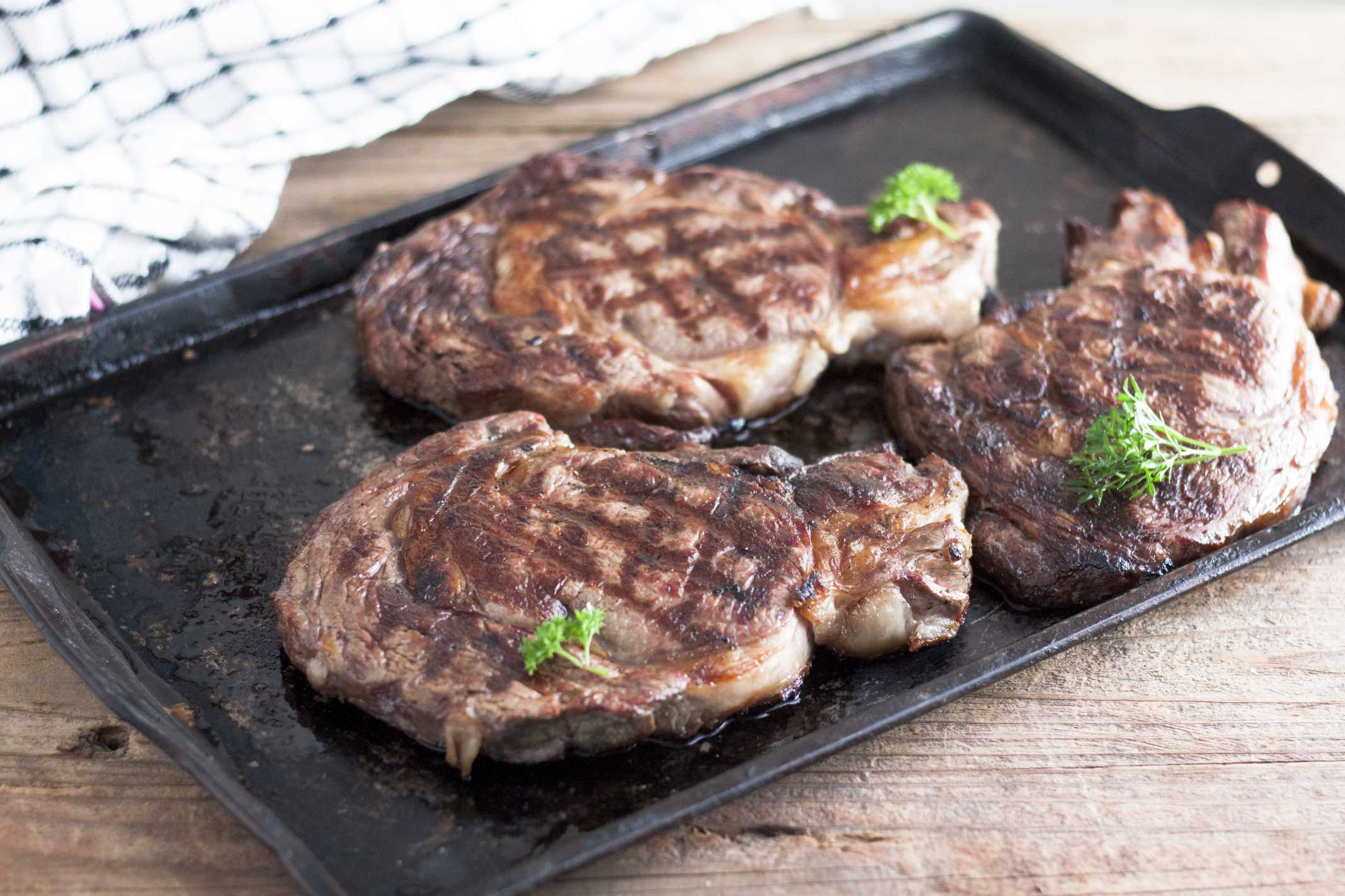 3 grilled steaks on a metal cookie tray.