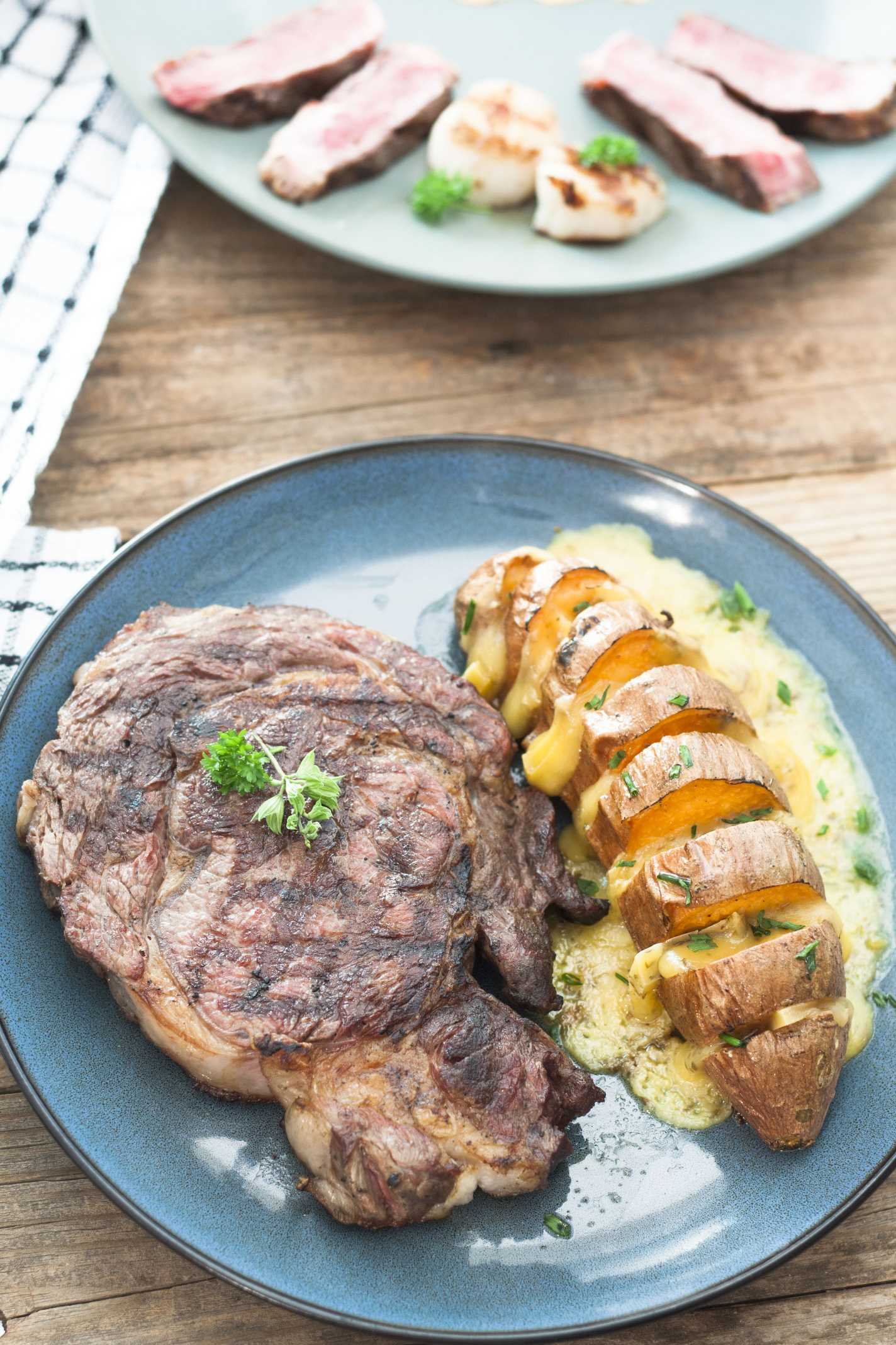 Hasselbeck Style Sweet Potatoes with puddle of melted cheese and large steak on blue plate