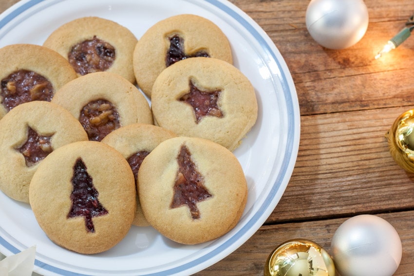 Jam filled cookies on white plate with Christmas Tree cutout, star cutout and circle cut out