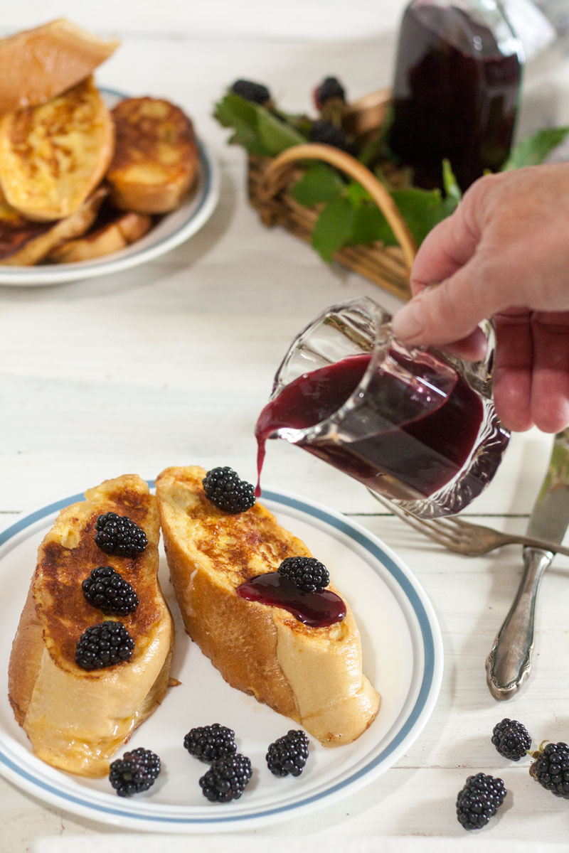 hand with blackberry syrup pouring on to French toast