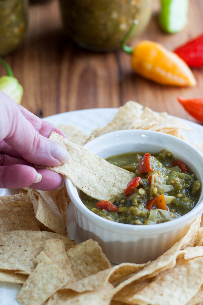 green tomato salsa in white bowl with hand scooping it on chip