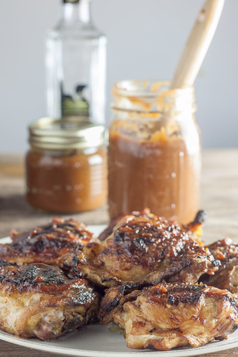 Platter with chicken thighs grilled with peach bourbon BBQ sauce with jar of salsa and bottle of bourbon