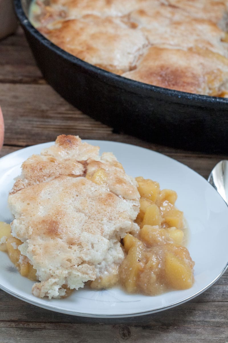 Peach Cobbler portion on white plate with cast iron skillet in background.