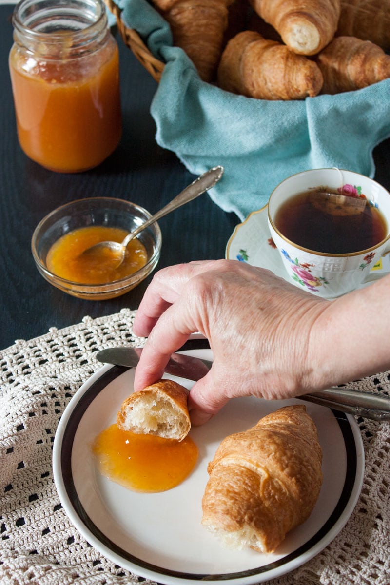 hand grabbing piece of croissant with low sugar peach jam 