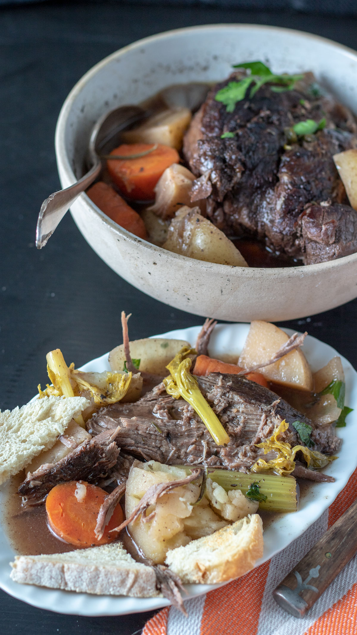 Serving of pot roast on white plate with serving bowl in background.