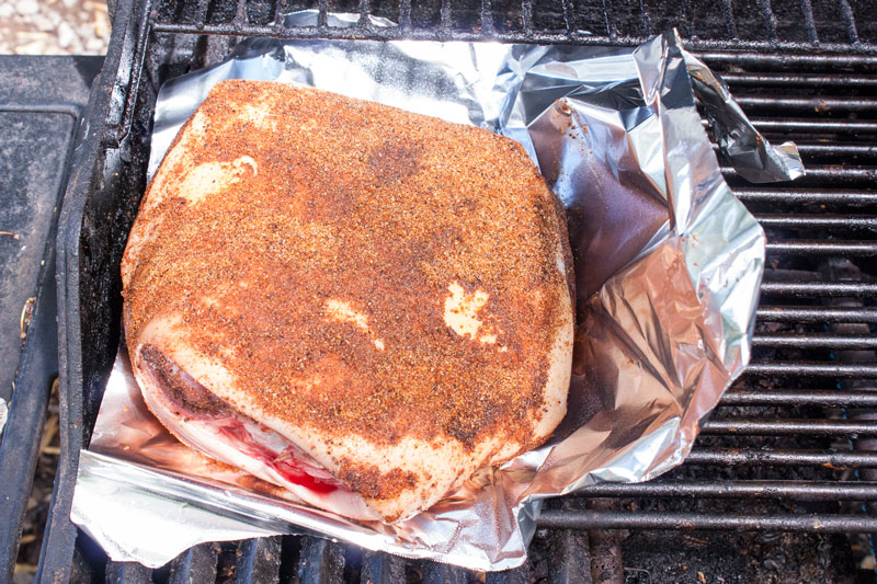 rubbed pork on grill protected by a piece of aluminum foil draped over the side