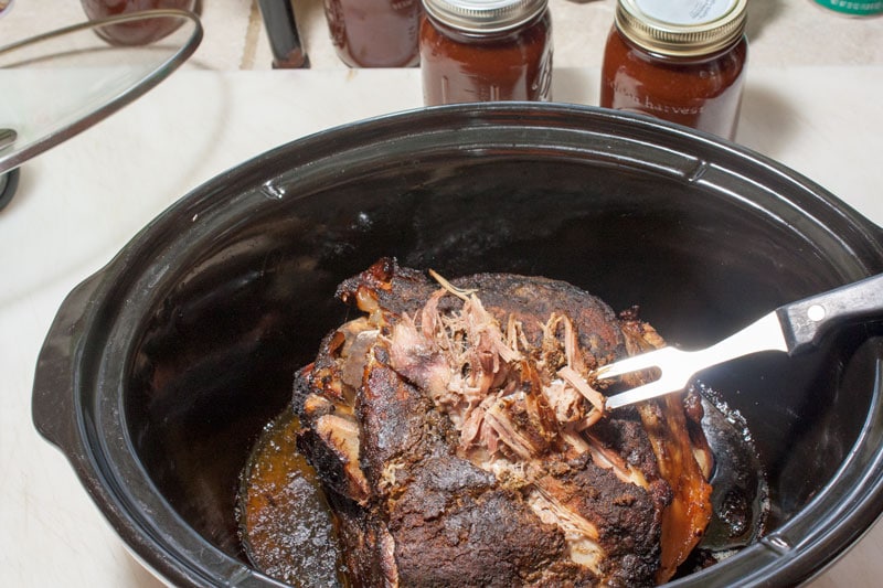 Pork roast in slow cooker with fork pulling the meat apart