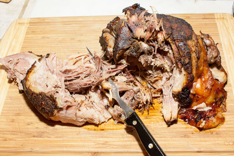 Pork roast pulled apart on bamboo cutting board.