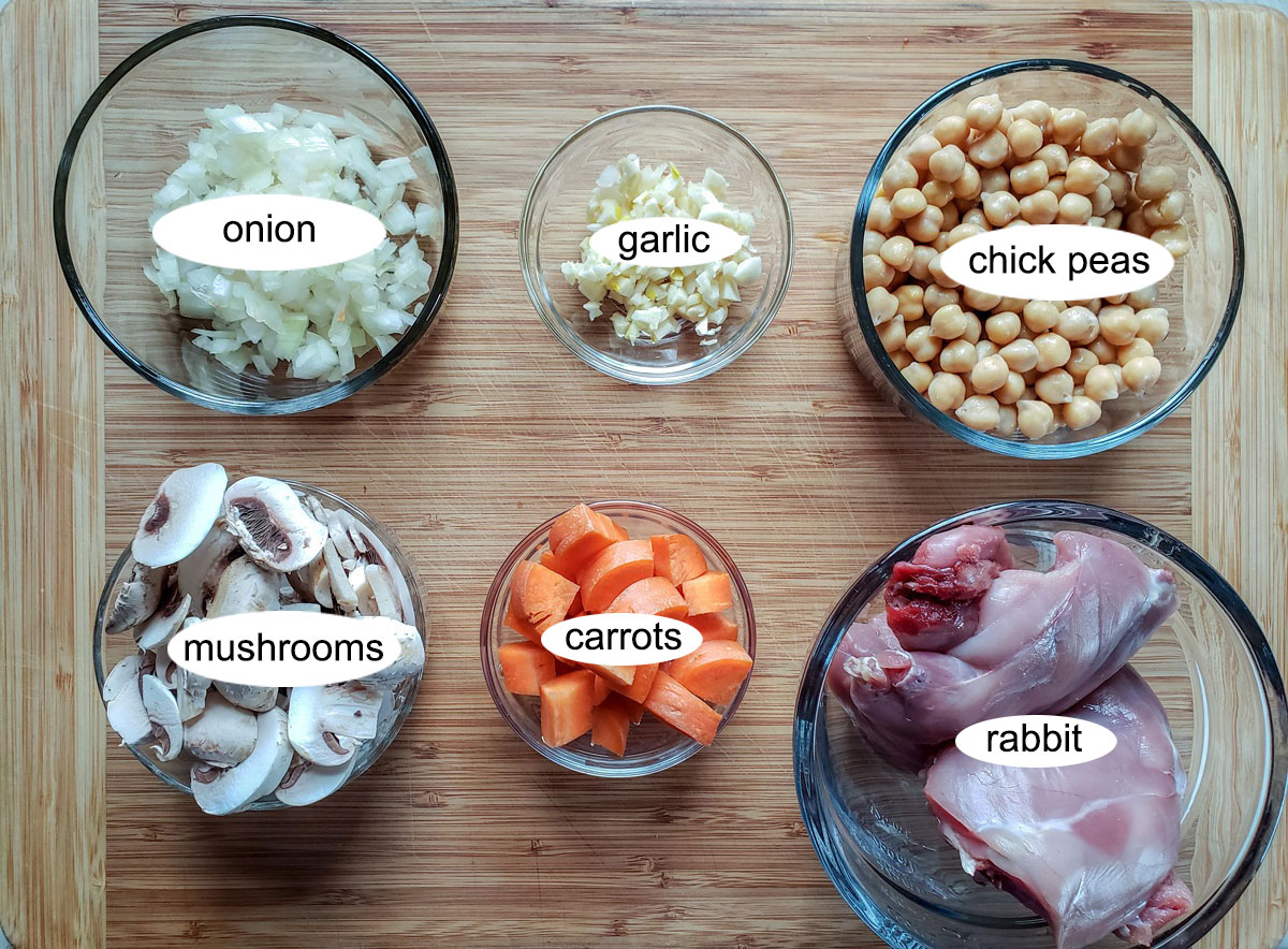 Rabbit, carrot, mushrooms, onions, garlic, chick peas in bowls on board
