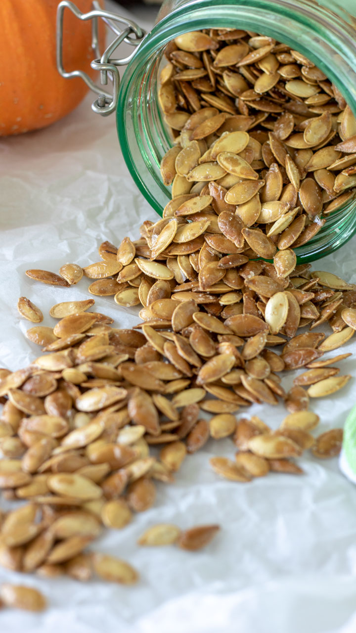 roasted pumpkins seeds in green jar on white board.