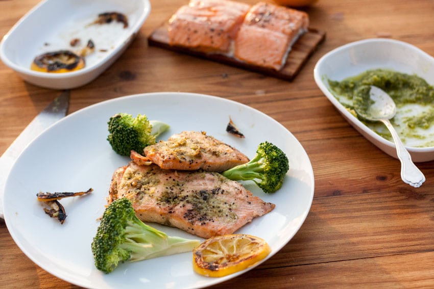 salmon with pesto on white plate with broccoli on wooden board