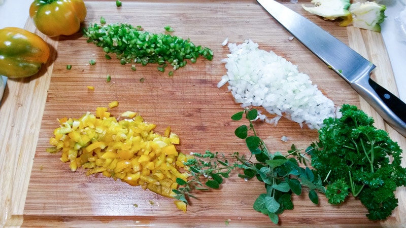 Chopped onion, yellow peppers, jalapeno, parsley and oregano on wooden cutting board.