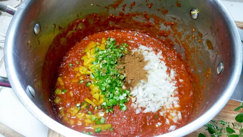 Pot with cooked down cherry tomatoes with peppers, onions, and spices.