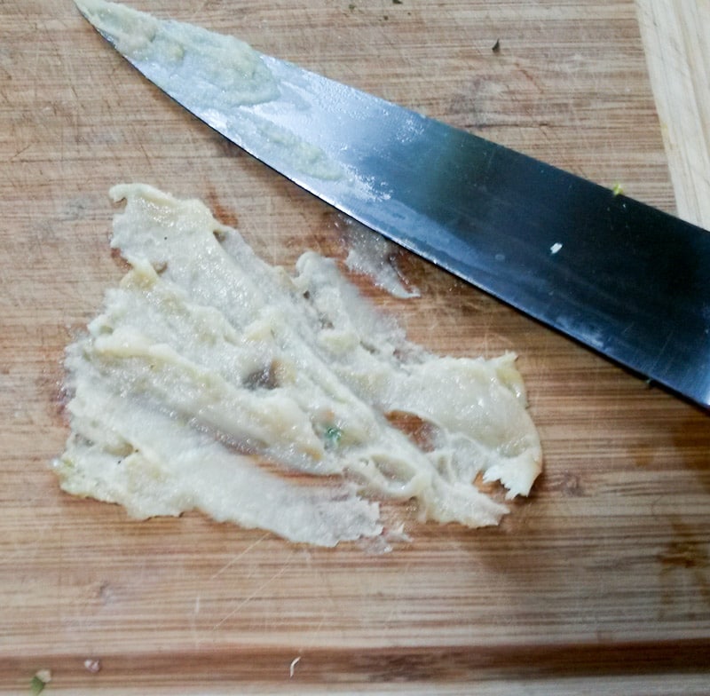 Roasted garlic smashed on wooden cutting board with chef's knife.