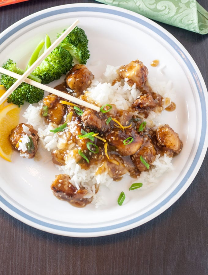Sesame Orange Chicken stir fry on white plate garnished with orange slices.