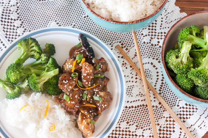 Sesame Orange Chicken stir fry on white plate with broccoli and rice.