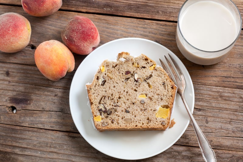 Peach Pecan Quick Bread on white plate with milk and peaches on the side. 