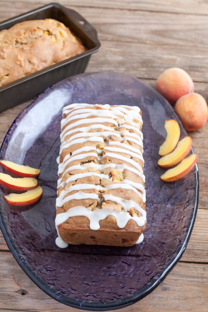 Glazed Peach Pecan Quick Bread on purple platter with sliced peaches.