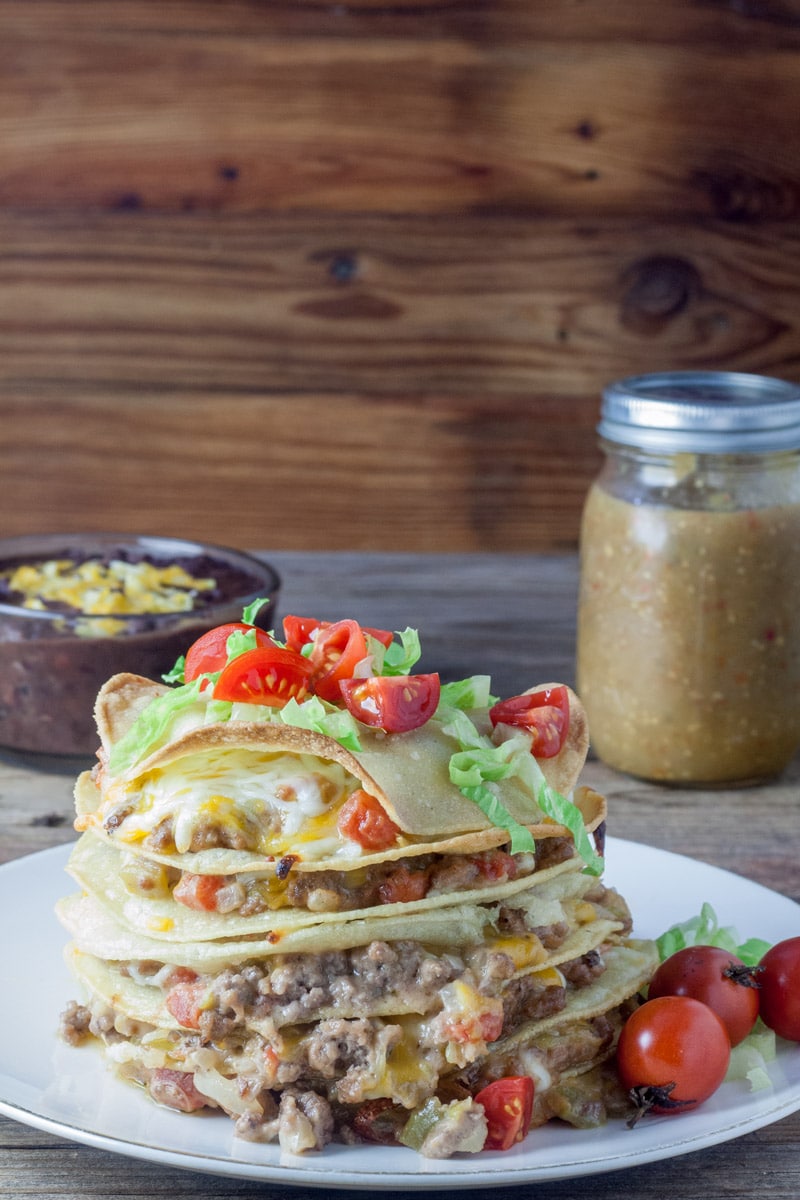 Tortillas stacked on top of each other with layers of beef and melted cheese, topped with tomatoes and lettuce.