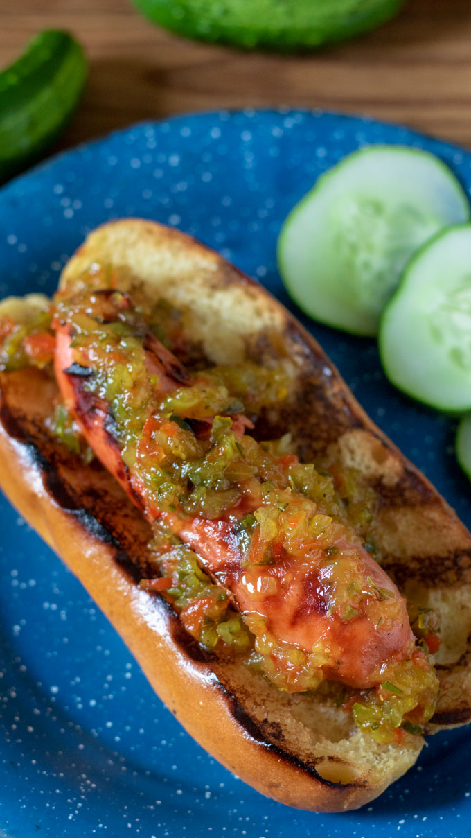 close up grilled hot dog and bun topped with sweet relish