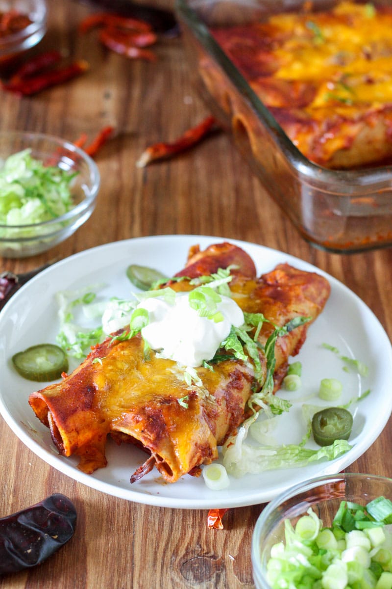 2 venison enchiladas on white plate with sour cream and garnishes