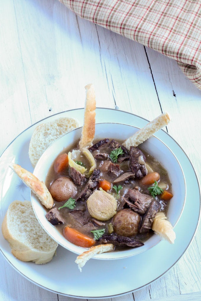 overhead shot of deer neck roast stew with slice French bread on white plate