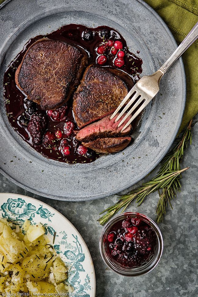 overhead photo of venison on pewter dish sitting on top red berry sauce