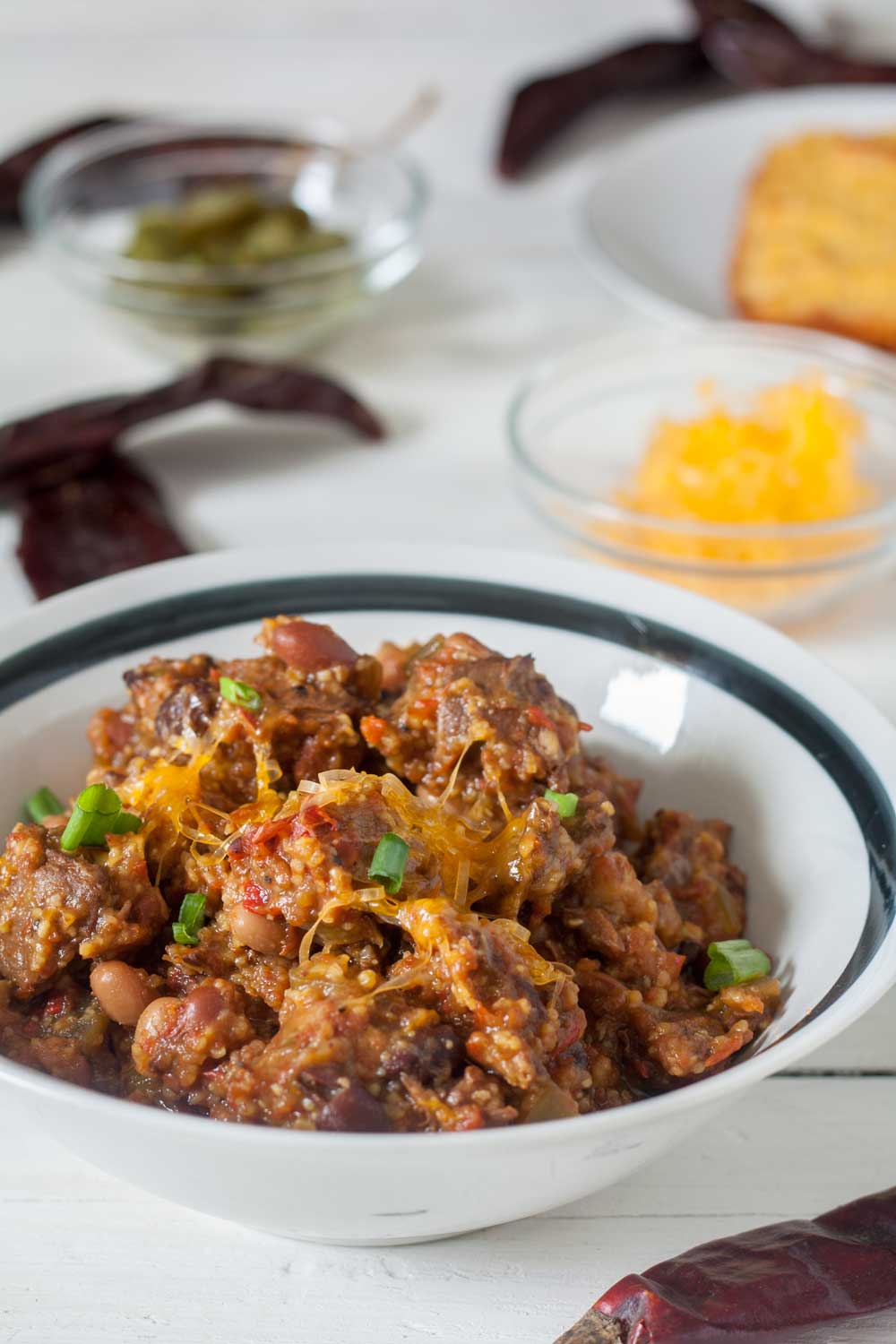 closeup chunky venison chili topped with scallions slices. and cheese